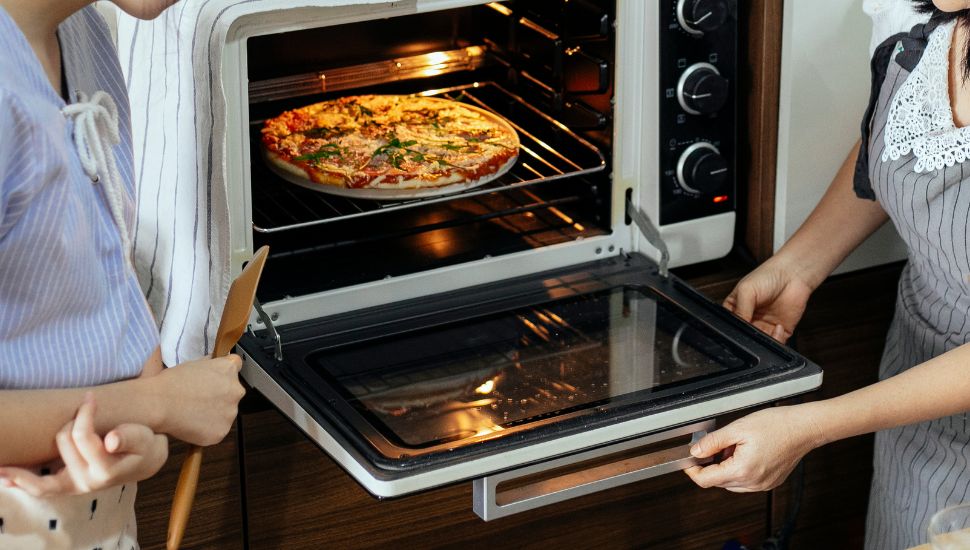 Image of two persons making a pizza in oven