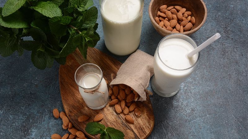 almond milk in glass and bottle with some almonds on side